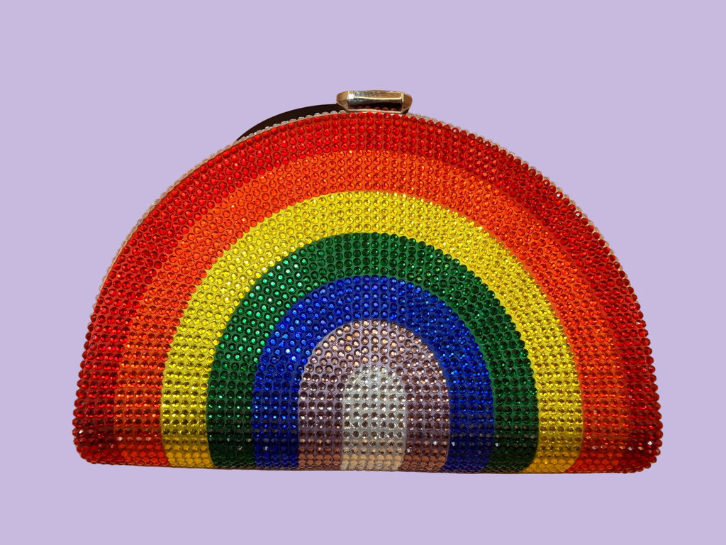 A semi-circular, rainbow-colored rhinestone clutch purse with a silver-tone metal clasp, displayed on a warm beige background.